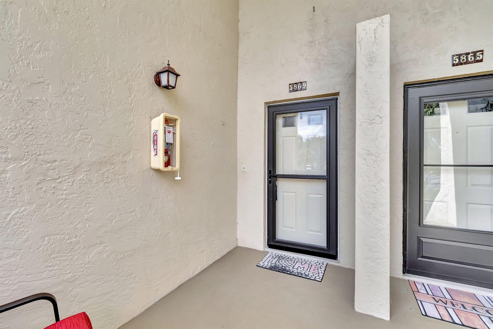 An exterior view of two adjacent apartment entry doors with a wall-mounted fire extinguisher — 5869 Parkwalk Drive, Boynton Beach FL 33472, BOYNTON BEACH, FL