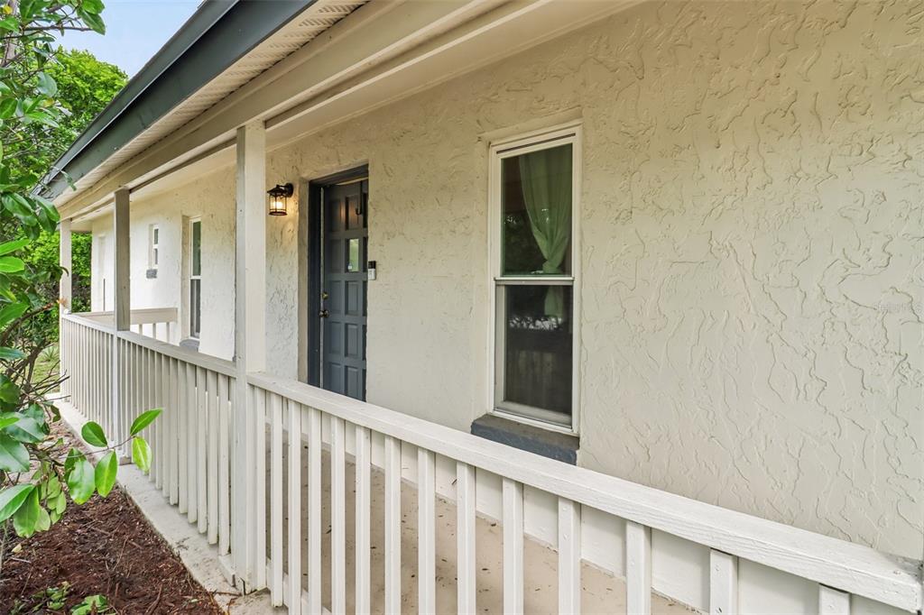 A covered porch with a white wooden railing runs along the side of a stucco house — 1200 E HANCOCK DRIVE, DELTONA, FL