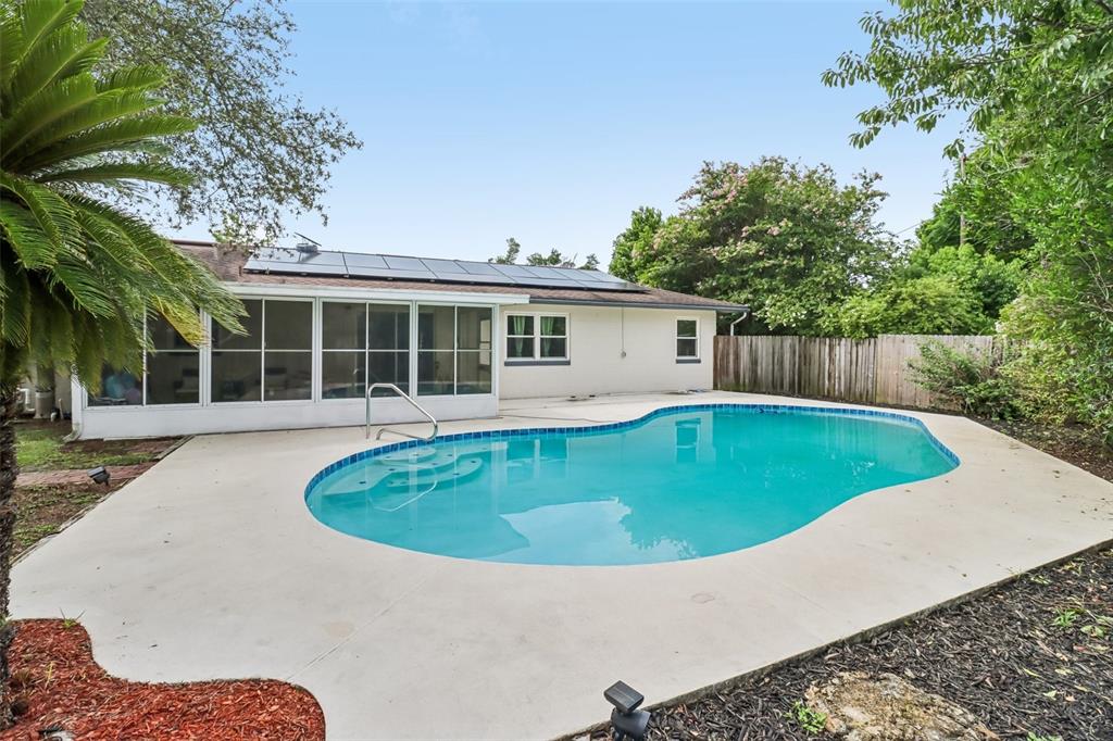 A backyard features a swimming pool with a concrete deck and a sunroom with solar panels — 1200 E HANCOCK DRIVE, DELTONA, FL
