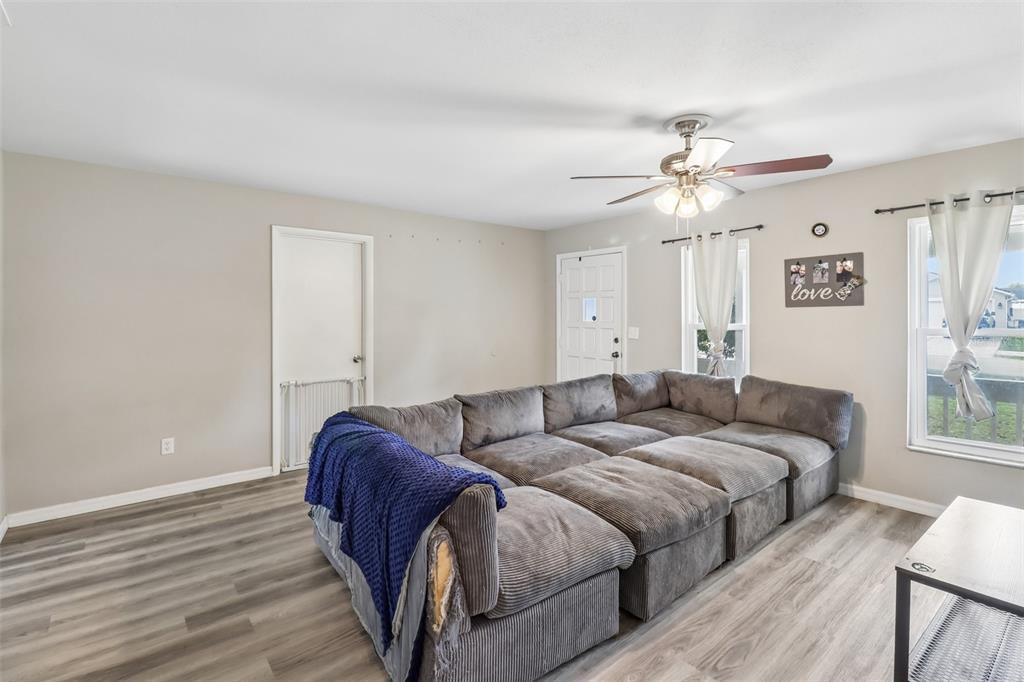 A living room features a large gray sectional sofa, wood-look flooring, and a ceiling fan — 1200 E HANCOCK DRIVE, DELTONA, FL