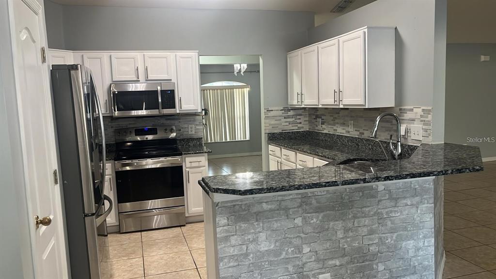 A kitchen features white cabinets, stainless steel appliances, granite countertops, and a faux-brick breakfast bar — 3116 KEYSTONE POINTE COURT, ST CLOUD, FL