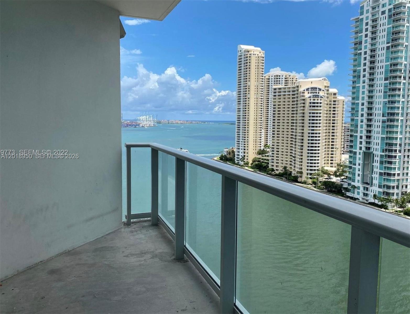 A balcony with a glass railing overlooks a bay and high-rise buildings — 300 S Biscayne Blvd # 1606, Miami FL 33131, MIAMI, FL