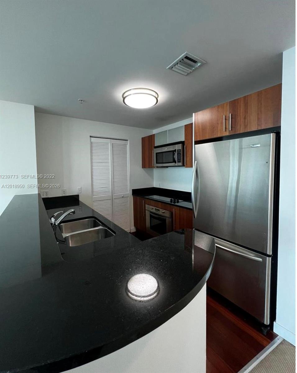 A kitchen features dark countertops, stainless steel appliances, and wood-toned cabinetry — 300 S Biscayne Blvd # 1606, Miami FL 33131, MIAMI, FL