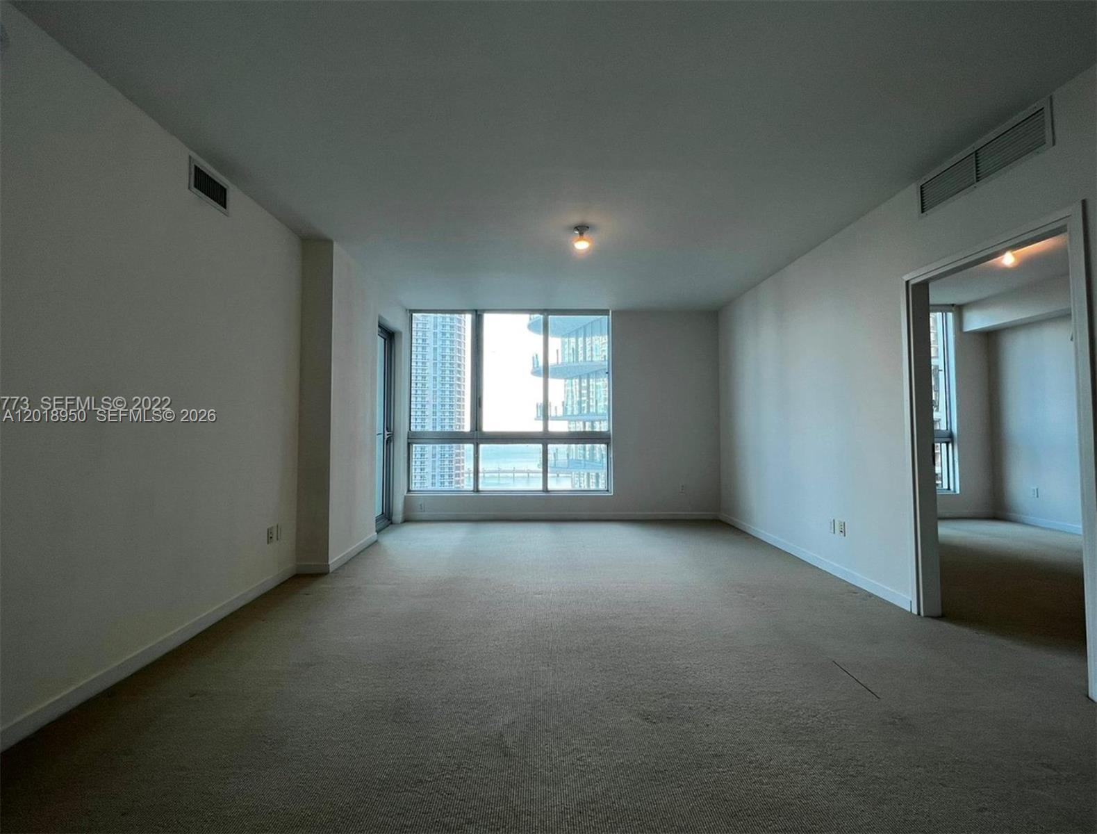 An empty room with beige carpeting, white walls, and large windows overlooking a city skyline — 300 S Biscayne Blvd # 1606, Miami FL 33131, MIAMI, FL