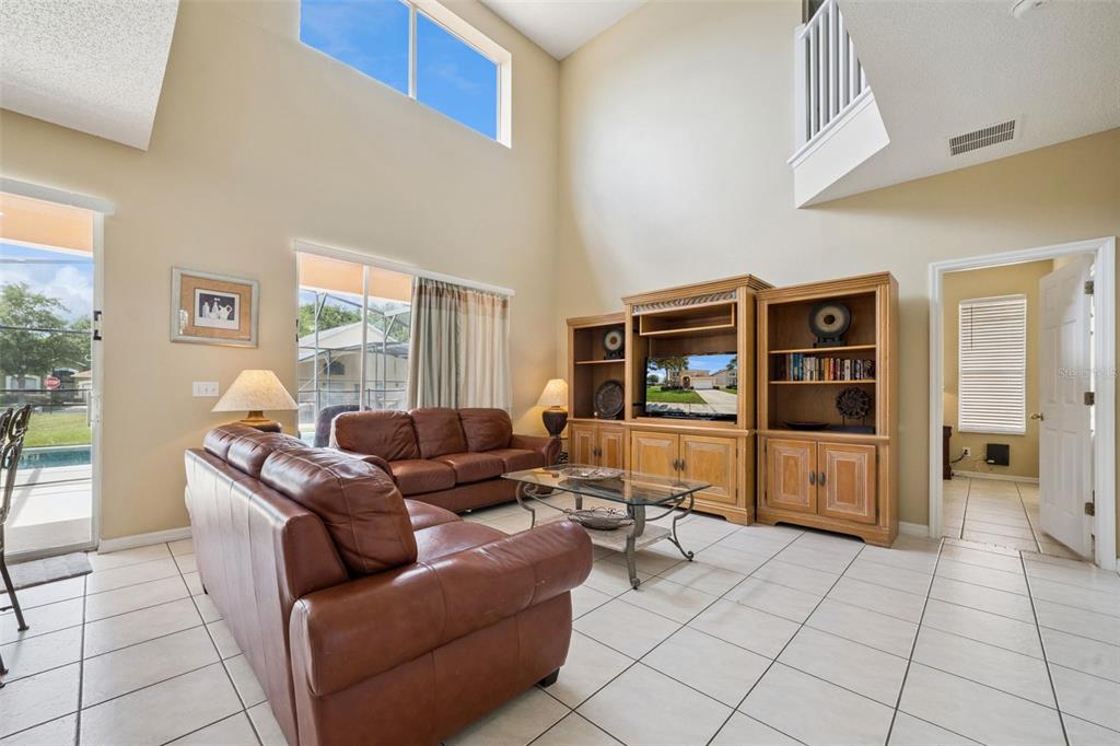 A living room with high ceilings, tile floors, leather sofas, and a large wooden entertainment center — 8550 SUNRISE KEY DRIVE, KISSIMMEE, FL