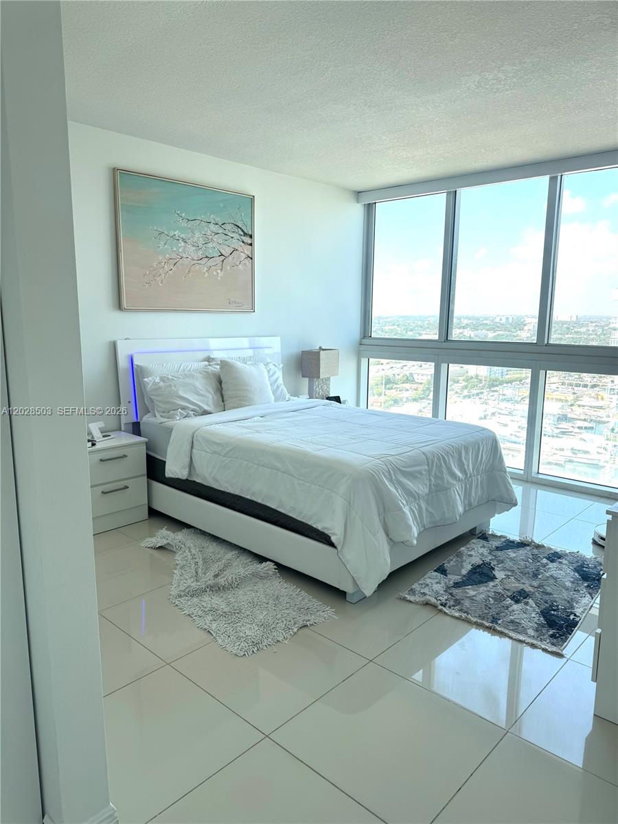 A bedroom features a white bed, a wall painting, and floor-to-ceiling windows with city views — 1861 NW S River Dr # 2201, Miami FL 33125, MIAMI, FL