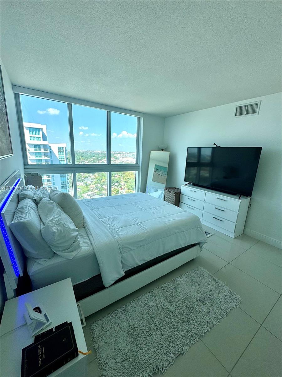 A bedroom with a bed, white dresser, large television, and floor-to-ceiling windows overlooking a city — 1861 NW S River Dr # 2201, Miami FL 33125, MIAMI, FL