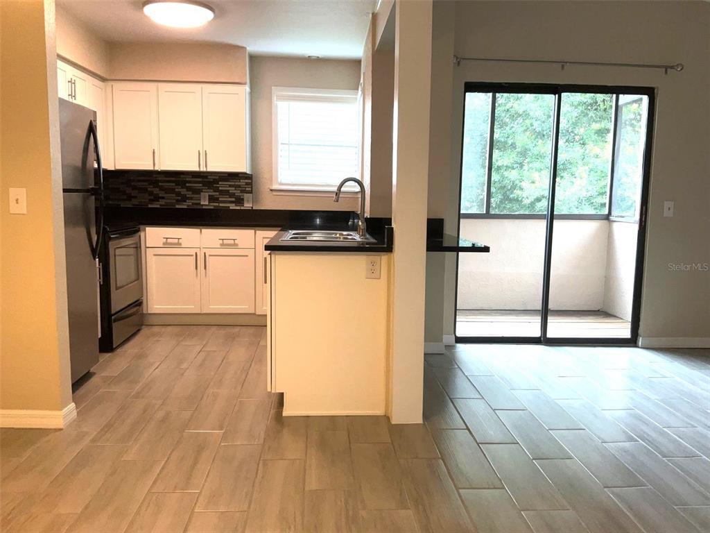 A kitchen with white cabinets, dark countertops, and tile flooring leads to a sliding glass door — 3014 ANTIQUE OAKS CIRCLE UNIT 120, WINTER PARK, FL