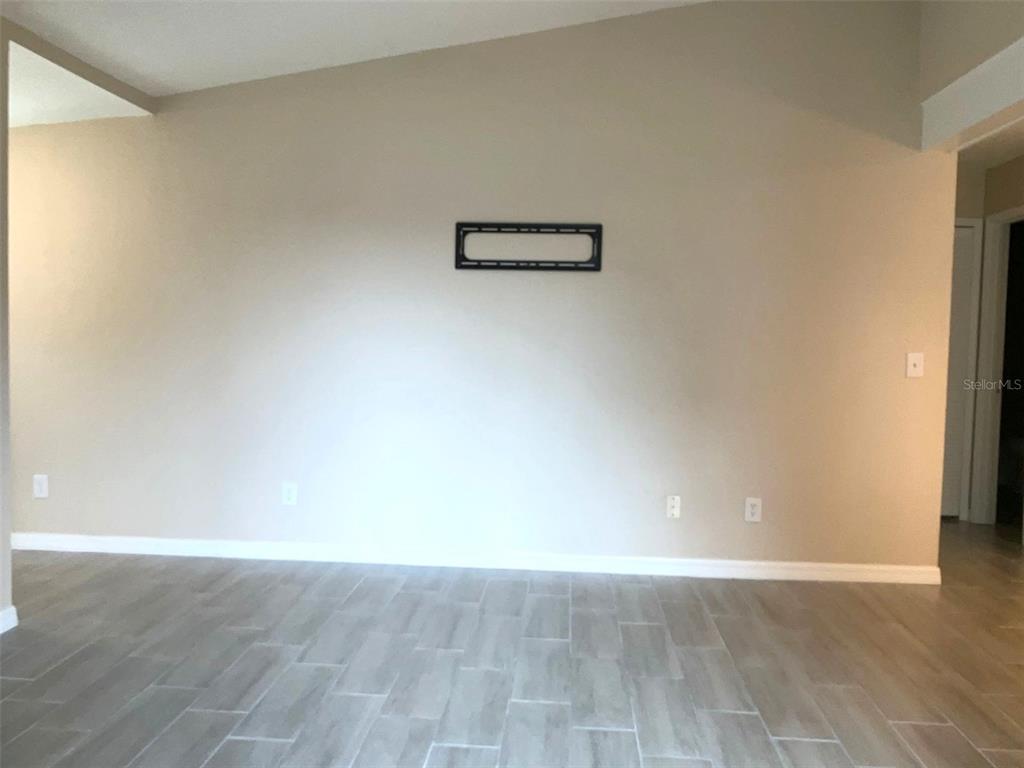 An empty room features light-colored walls, wood-look tile flooring, and a wall-mounted television bracket — 3014 ANTIQUE OAKS CIRCLE UNIT 120, WINTER PARK, FL