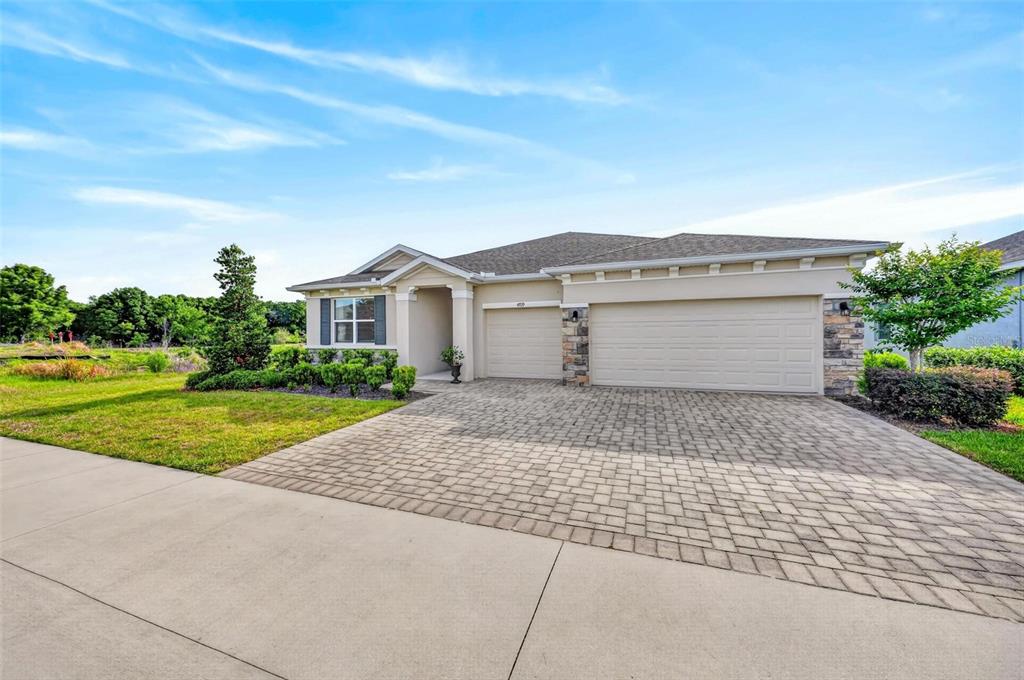 A single-story house with a paved driveway, three-car garage, and stone accents under a blue sky — 4709 NW 51ST COURT, OCALA, FL