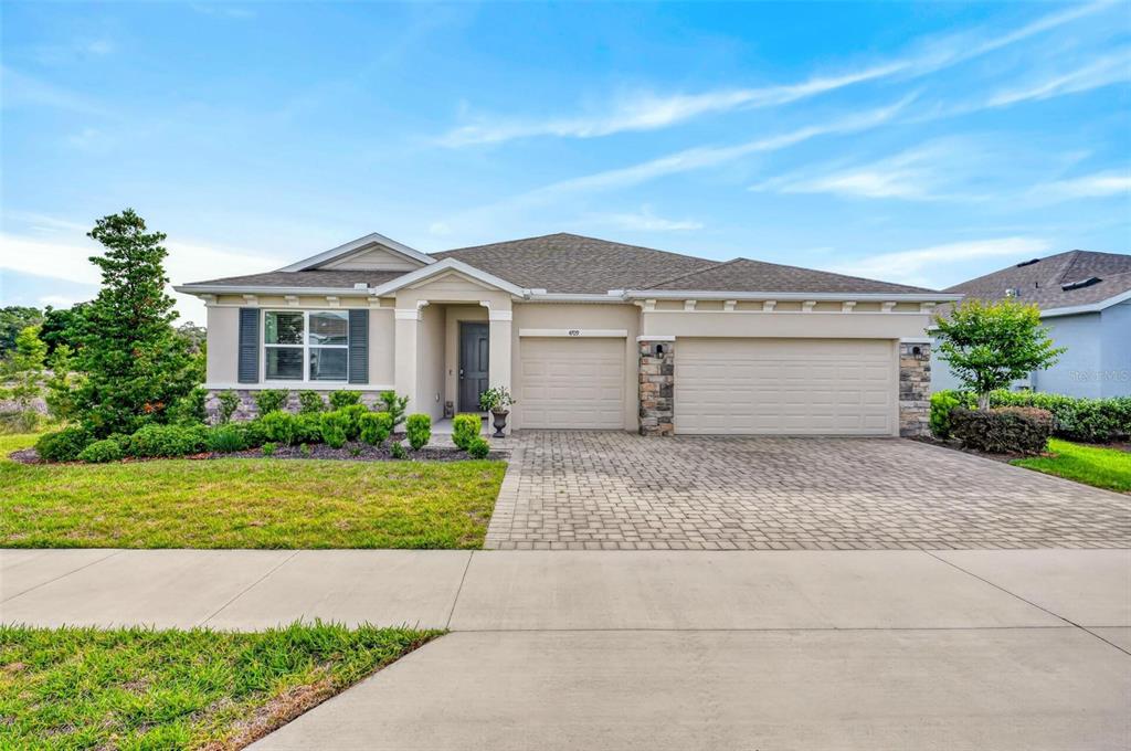 A single-story house with a beige stucco exterior, stone accents, and a three-car garage — 4709 NW 51ST COURT, OCALA, FL