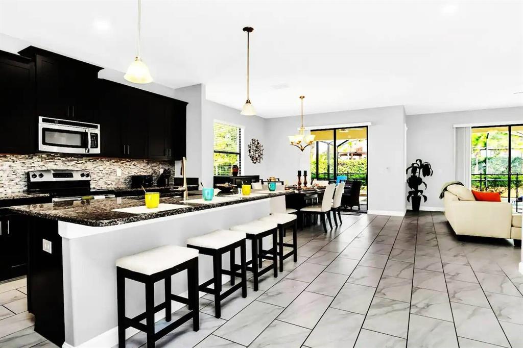 A modern kitchen with dark cabinets, granite countertops, and a breakfast bar overlooks a dining area — 5504 SOLTERRA CIRCLE, DAVENPORT, FL
