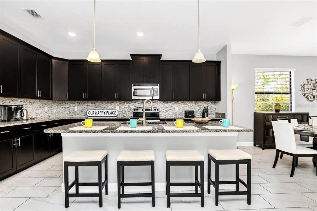 A kitchen features dark wood cabinets, granite countertops, a central island with four stools, and tile flooring — 5504 SOLTERRA CIRCLE, DAVENPORT, FL