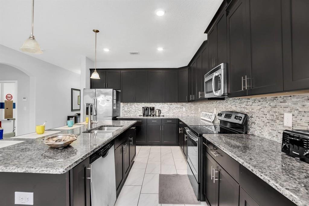 A kitchen features dark cabinets, granite countertops, stainless steel appliances, and a tiled backsplash — 5504 SOLTERRA CIRCLE, DAVENPORT, FL