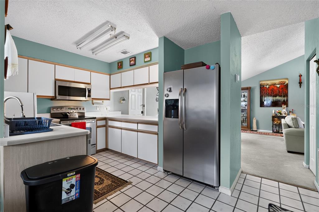 A kitchen with white cabinets, stainless steel appliances, and tile flooring opens to a living area — 44 WEDGEWOOD LANE, PALM COAST, FL