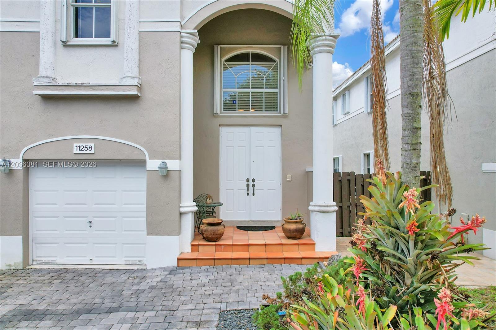 The exterior of a two-story home features a white double door, garage, and arched window — 11258 NW 47th Ln, Doral FL 33178, DORAL, FL