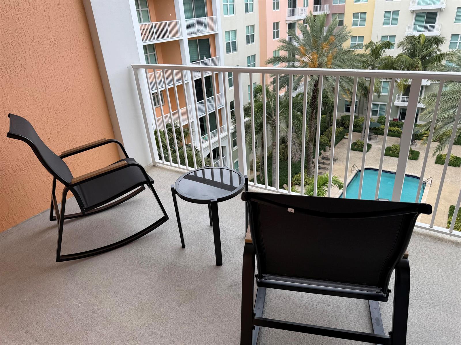 A balcony with two rocking chairs and a small table overlooks a pool area — 804 E Windward Way # 618, Lantana FL 33462, LANTANA, FL