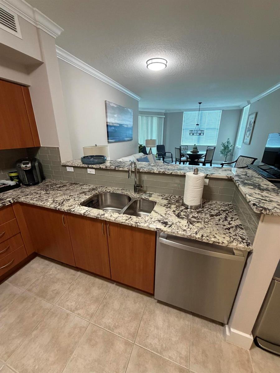 A kitchen with wood cabinets, granite countertops, and a stainless steel dishwasher overlooks a dining area — 804 E Windward Way # 618, Lantana FL 33462, LANTANA, FL