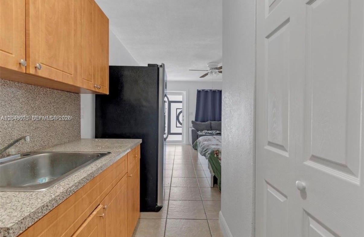 A kitchen with wood cabinets and a stainless steel sink leads into a bedroom area — 329 W 18th St, Hialeah FL 33010, HIALEAH, FL