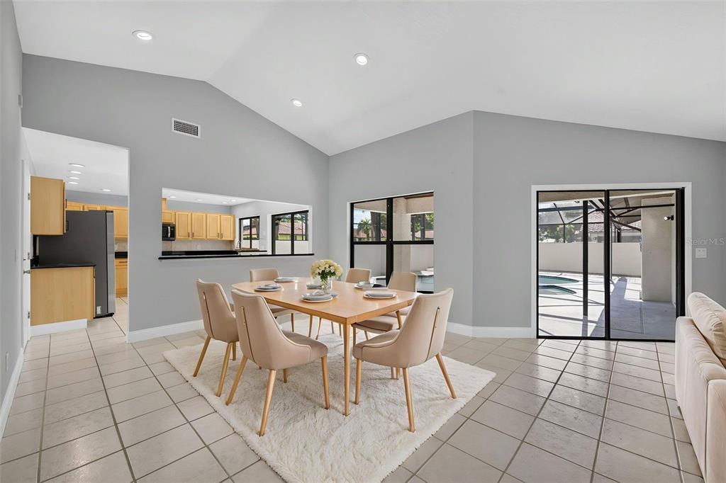 A dining room with a light wood table, beige chairs, tile floors, and pool access — 8052 S CADIZ COURT, ORLANDO, FL