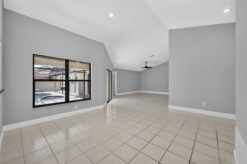 An empty room with light gray walls, tile flooring, vaulted ceilings, and a large window — 8052 S CADIZ COURT, ORLANDO, FL