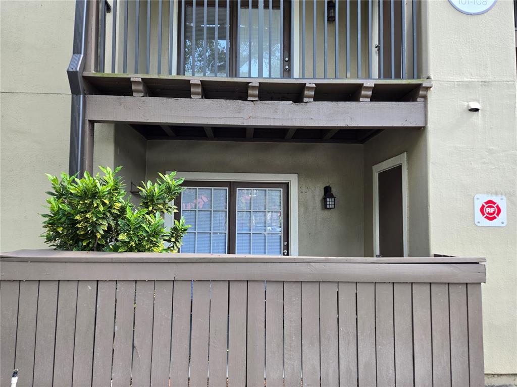A ground-level patio with a wooden fence, a sliding glass door, and an upper balcony — 234 AFTON SQUARE UNIT 103, ALTAMONTE SPRINGS, FL