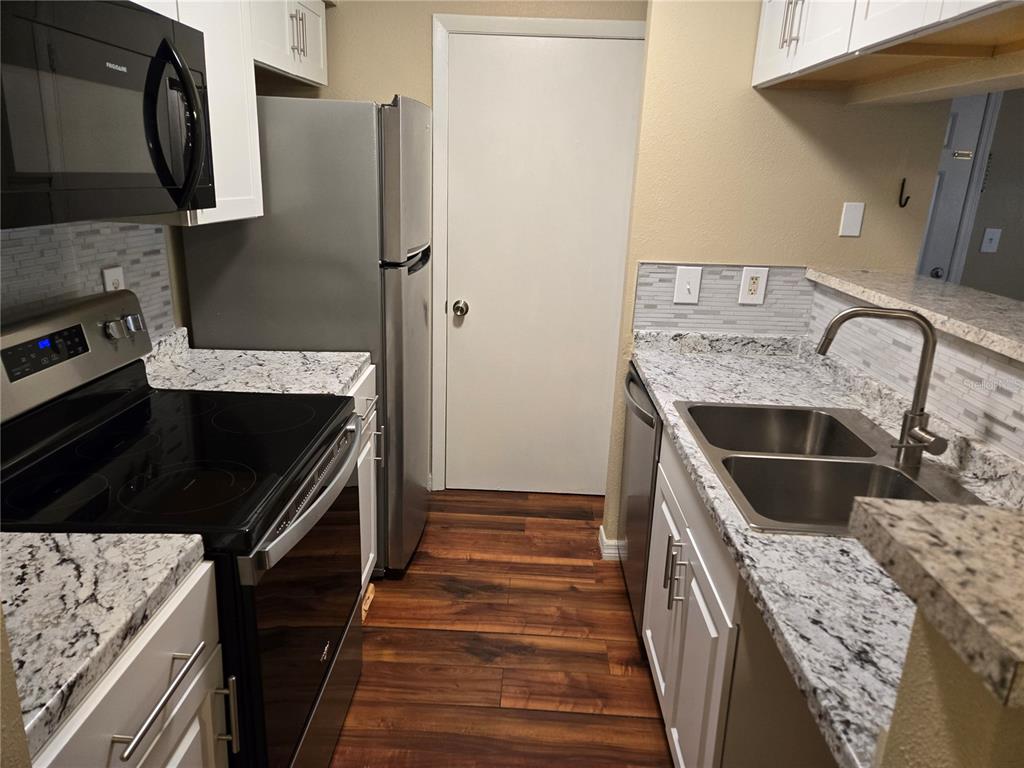 A galley kitchen features white cabinets, granite countertops, stainless steel appliances, and wood-look flooring — 234 AFTON SQUARE UNIT 103, ALTAMONTE SPRINGS, FL