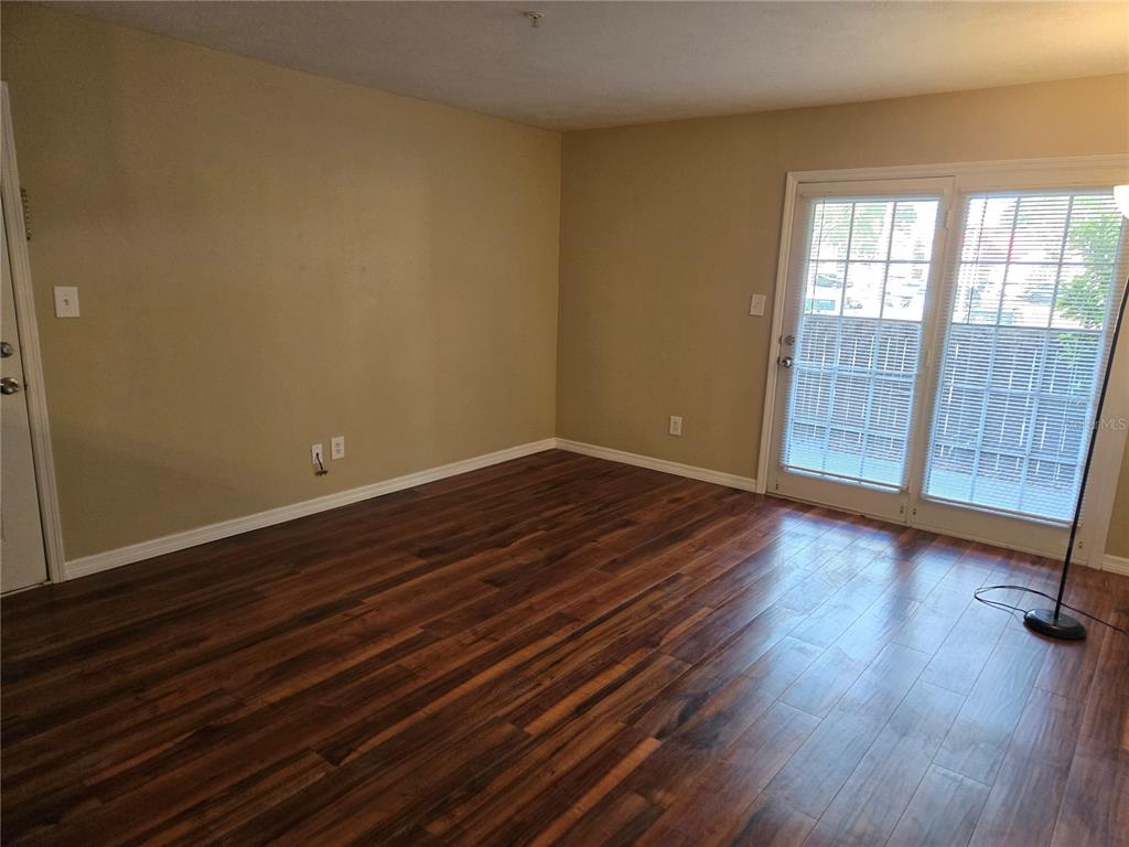 An empty room features dark wood-look flooring, beige walls, and sliding glass doors — 234 AFTON SQUARE UNIT 103, ALTAMONTE SPRINGS, FL