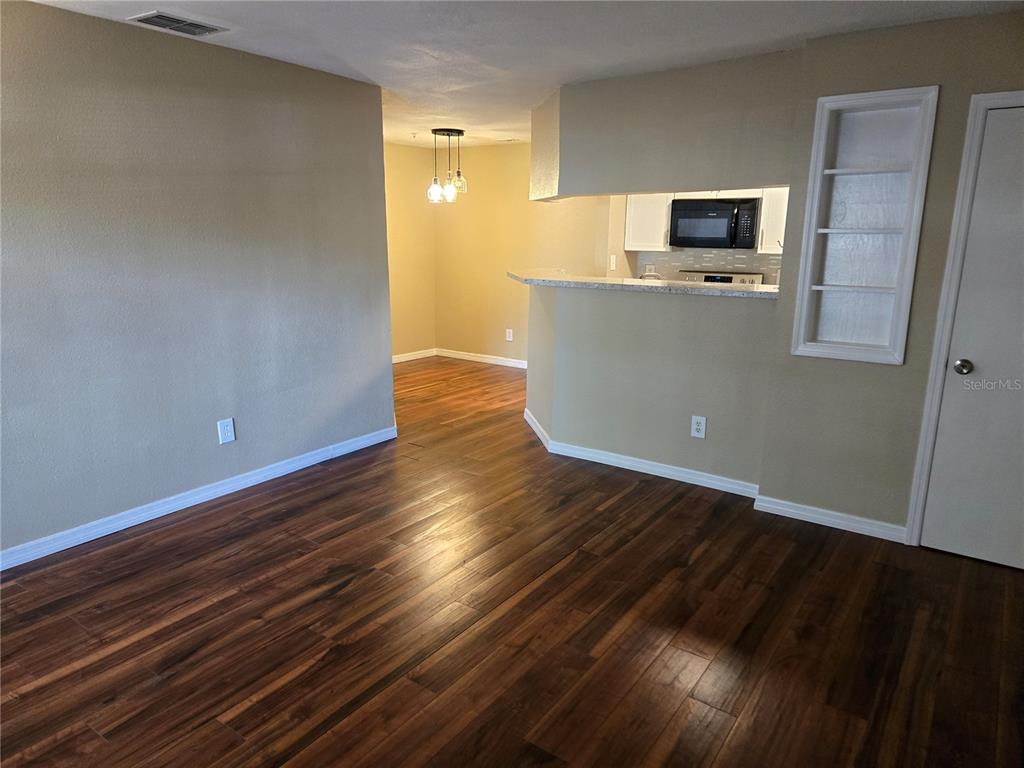 A living area with wood-look flooring leads to a kitchen with a breakfast bar — 234 AFTON SQUARE UNIT 103, ALTAMONTE SPRINGS, FL