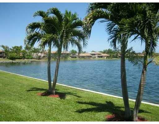 Two palm trees stand on a grassy lawn overlooking a lake with houses in distance — 443 NE 195th St # 345, Miami FL 33179, MIAMI, FL