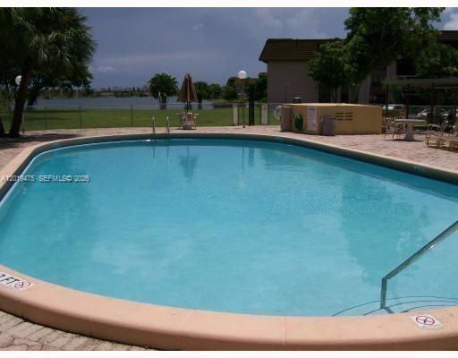 An outdoor swimming pool with a tan coping edge overlooks a grassy area and lake — 443 NE 195th St # 345, Miami FL 33179, MIAMI, FL