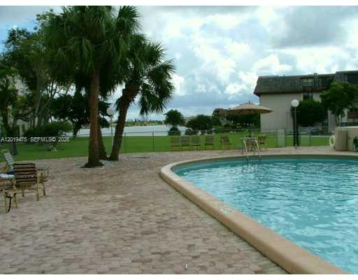 A swimming pool with a paved deck, palm trees, and a building in the background — 443 NE 195th St # 345, Miami FL 33179, MIAMI, FL