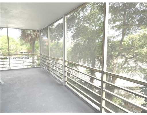 A screened-in balcony with a concrete floor overlooks trees and a body of water — 443 NE 195th St # 345, Miami FL 33179, MIAMI, FL