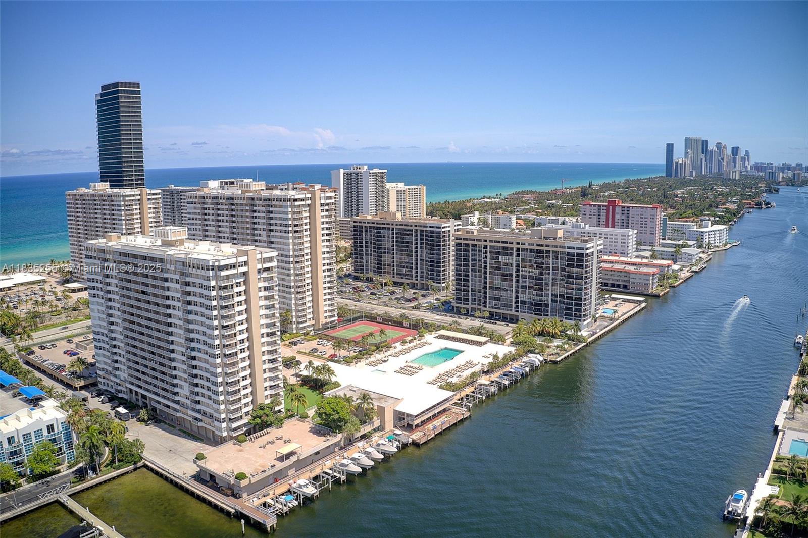 An aerial view shows high-rise apartment buildings, a swimming pool, tennis courts, and a canal — 1945 S Ocean Dr # 901, Hallandale Beach FL 33009, HALLANDALE BEACH, FL