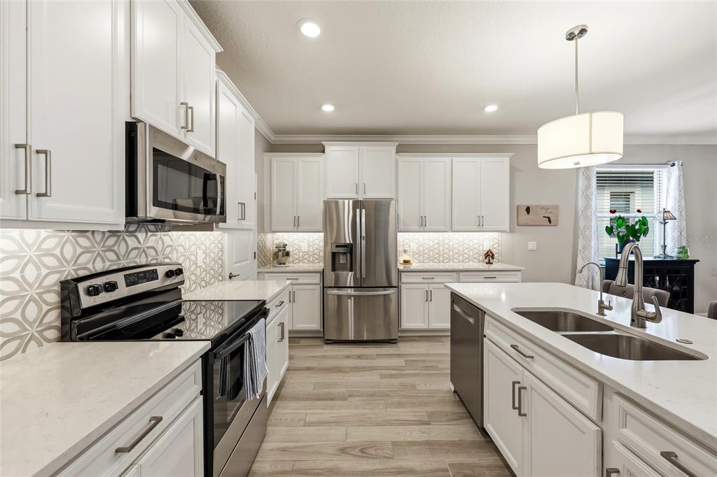 A modern kitchen features white cabinets, stainless steel appliances, quartz countertops, and patterned tile backsplash — 31553 CANNON RUSH DRIVE, SAN ANTONIO, FL