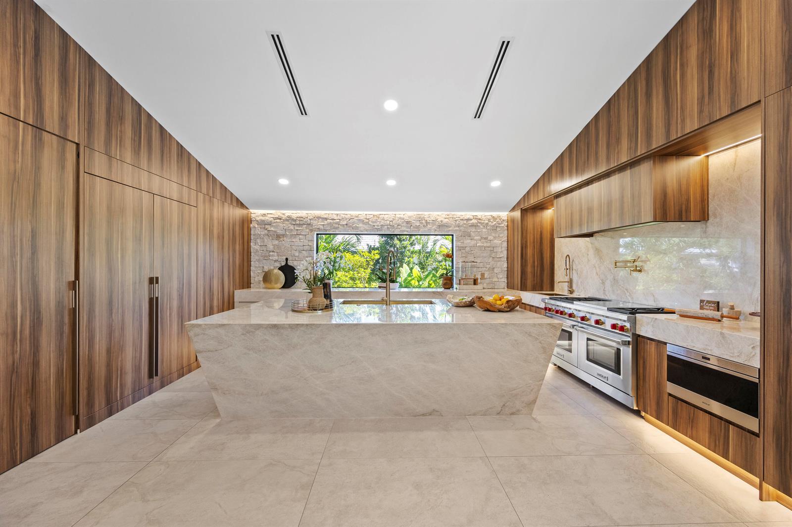 A modern kitchen features a large stone island, wood cabinetry, and a view of greenery — 10290 Silver Lake Drive, Boca Raton FL 33428, BOCA RATON, FL