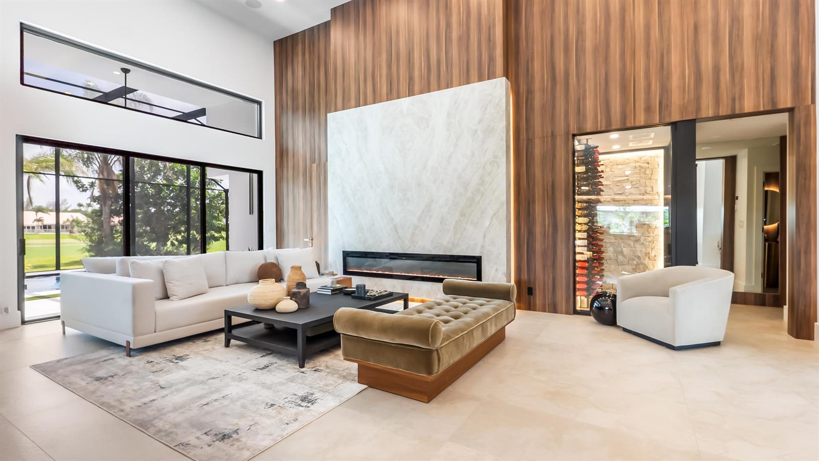 A modern living room features a marble fireplace, wood-paneled walls, a wine cellar, and large windows — 10290 Silver Lake Drive, Boca Raton FL 33428, BOCA RATON, FL