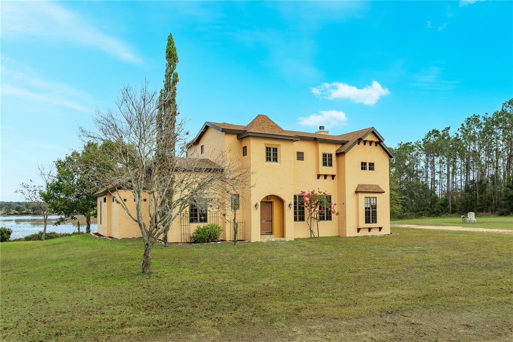 A two-story yellow stucco house with a brown roof sits on a grassy lot — 24540 TURKEY LAKE ROAD, HOWEY IN THE HILLS, FL