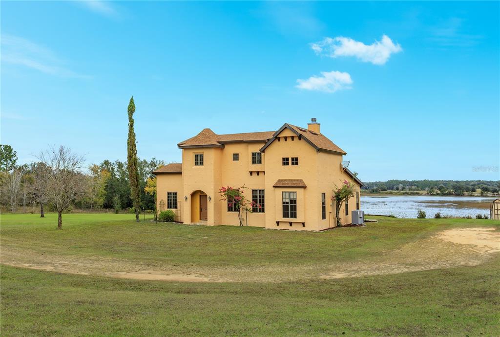 A two-story yellow stucco house sits on a grassy lot near a lake — 24540 TURKEY LAKE ROAD, HOWEY IN THE HILLS, FL