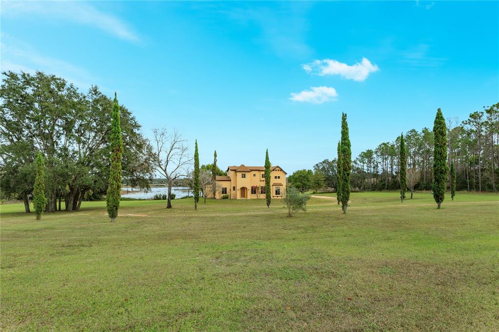 A two-story tan stucco house sits on a large grassy lot near a lake — 24540 TURKEY LAKE ROAD, HOWEY IN THE HILLS, FL