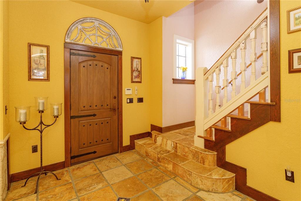 An entryway features a wooden door, stone tile flooring, and a staircase with white railings — 24540 TURKEY LAKE ROAD, HOWEY IN THE HILLS, FL