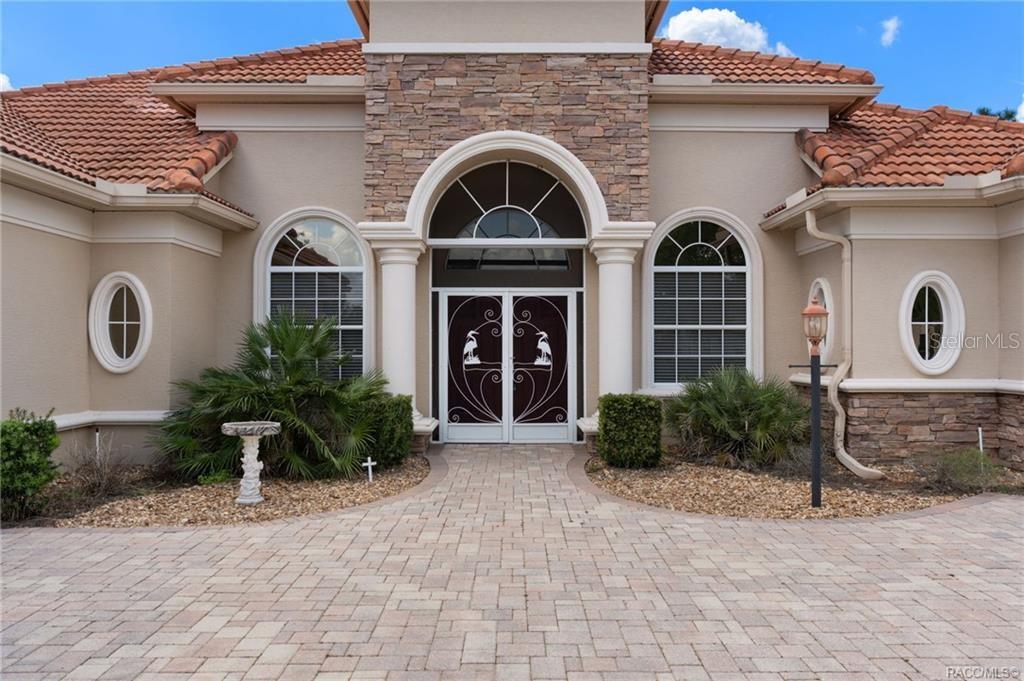 The exterior of a house features a stone-accented entryway, arched windows, and a paved driveway — 291 S PALADINN CIRCLE, INVERNESS, FL