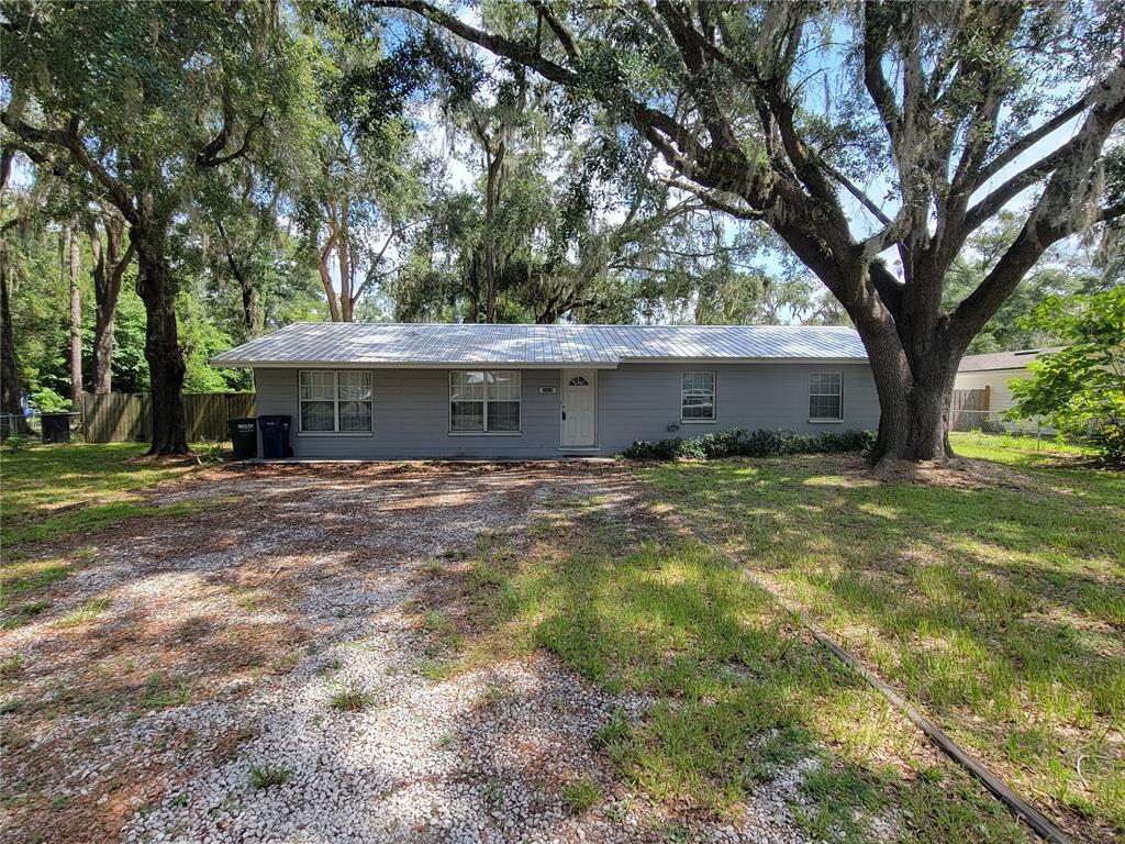 A single-story gray house with a metal roof sits behind a gravel driveway and trees — 26424 SW 1 AVENUE, NEWBERRY, FL