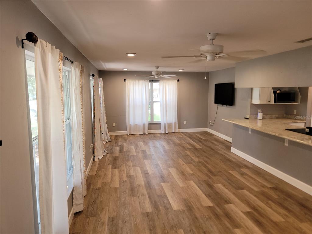 A living room with wood-look flooring, white curtains, ceiling fans, and an open kitchen counter — 26424 SW 1 AVENUE, NEWBERRY, FL