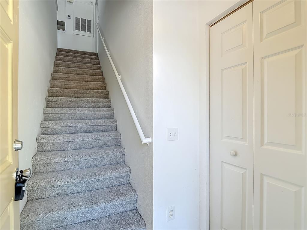 A carpeted staircase leads upward next to a white closet door and a light switch — 36106 LAKE CHASE BOULEVARD Unit 201, ZEPHYRHILLS, FL