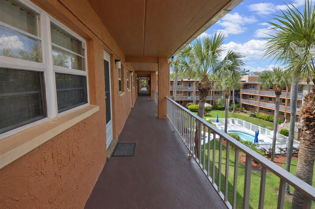 An outdoor apartment walkway overlooks a swimming pool and courtyard with palm trees — 12760 INDIAN ROCKS ROAD UNIT 573, LARGO, FL