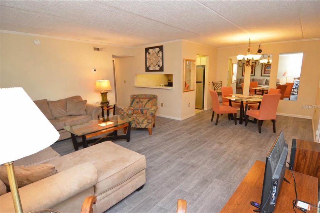 A living room and dining area with light wood-look flooring and a pass-through kitchen window — 12760 INDIAN ROCKS ROAD UNIT 573, LARGO, FL