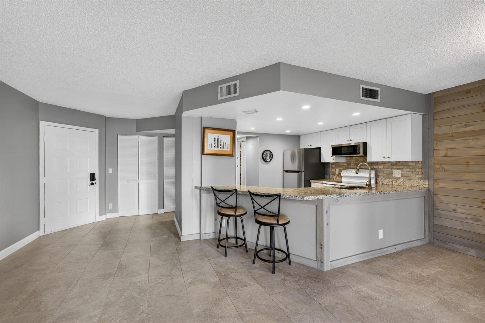 A kitchen with white cabinets, granite countertops, and a breakfast bar with two stools — 1605 S Us Highway 1 # D105, Jupiter FL 33477, JUPITER, FL