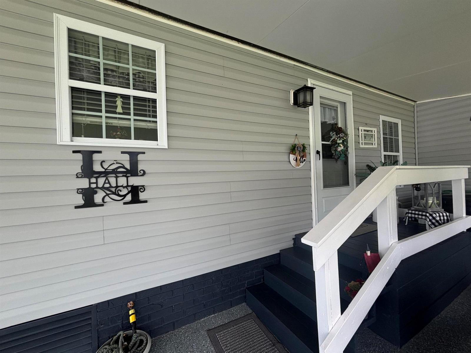 A gray vinyl-sided house exterior features a white front door, porch stairs, and metal signage — 1529 SW 35th Circle, Okeechobee FL 34974, OKEECHOBEE, FL