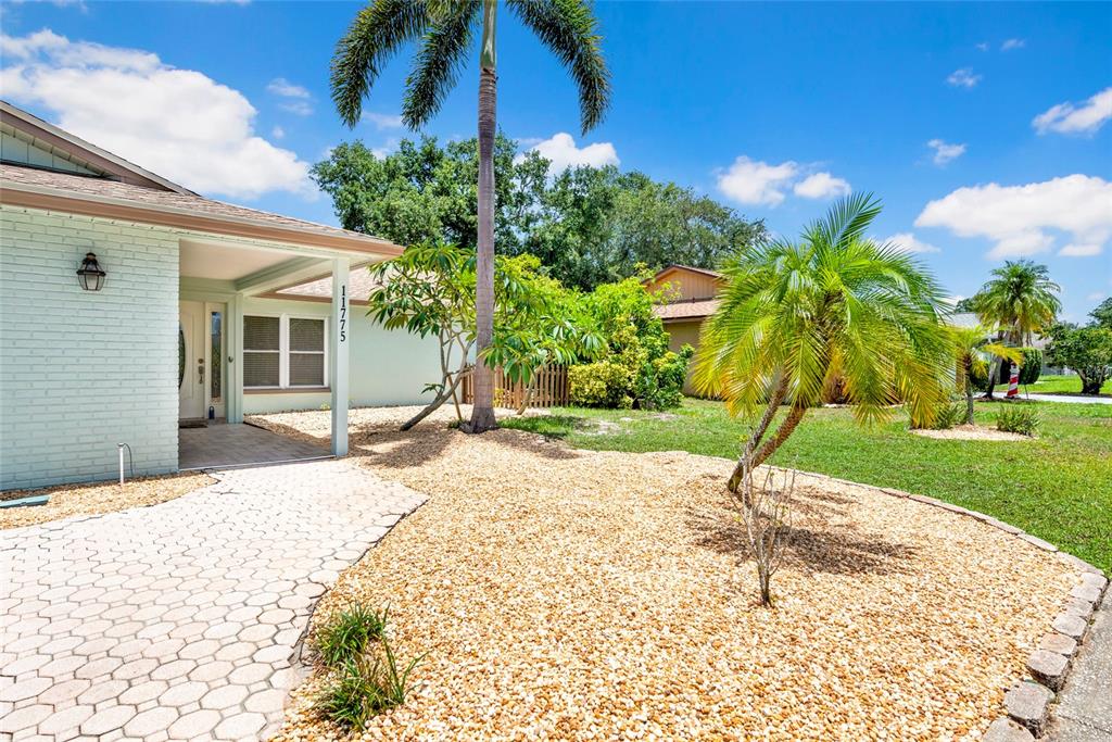 A light-colored brick house features a paved walkway, gravel landscaping, and several palm trees — 11775 112TH AVENUE, SEMINOLE, FL